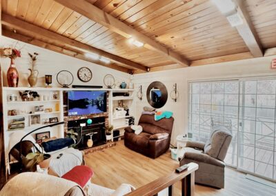 Living room with wooden ceiling, multiple recliners, a TV, bookshelves, wall clocks, and large glass doors opening to the outside.